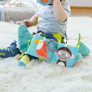 Otrok, ki se igra z mehko knjigo v obliki krokodila z barvnimi živalskimi aplikacijami, med sedenjem na preprogi.