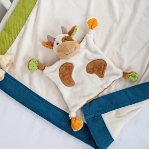 Ninica v obliki kravice položena na postelji s plišasto odejo.