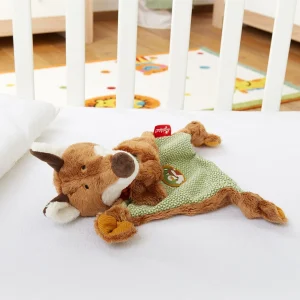 Ninica lisica Sigikid, ki leži v otroški posteljici poleg odeje.