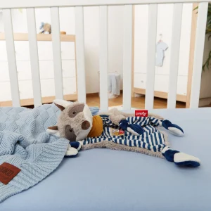 Ninica rakun Sigikid, ki leži v otroški posteljici poleg odejice.